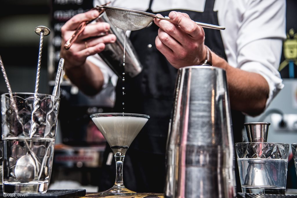 bartender pours a cocktail from a shaker through a sieve